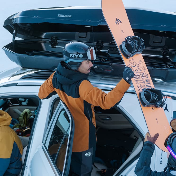 person putting snowboard into opened up CBX cargo box on top of vehicle