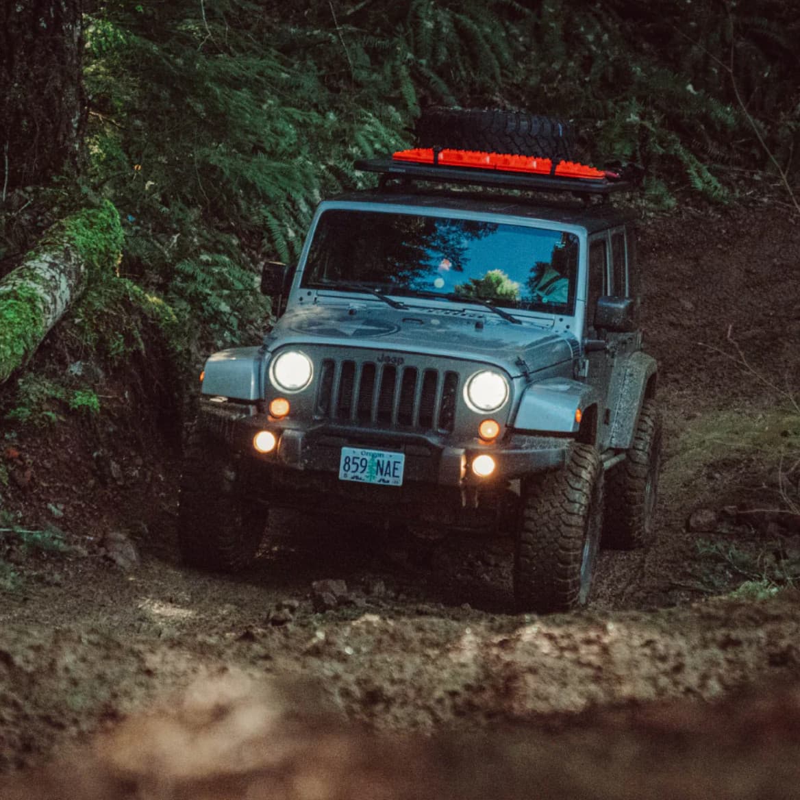 Lifestyle picture of Jeep JK outfitted with Yakima RibCage, LockNLoad platform, spare tire and recovery boards off-roading in forest