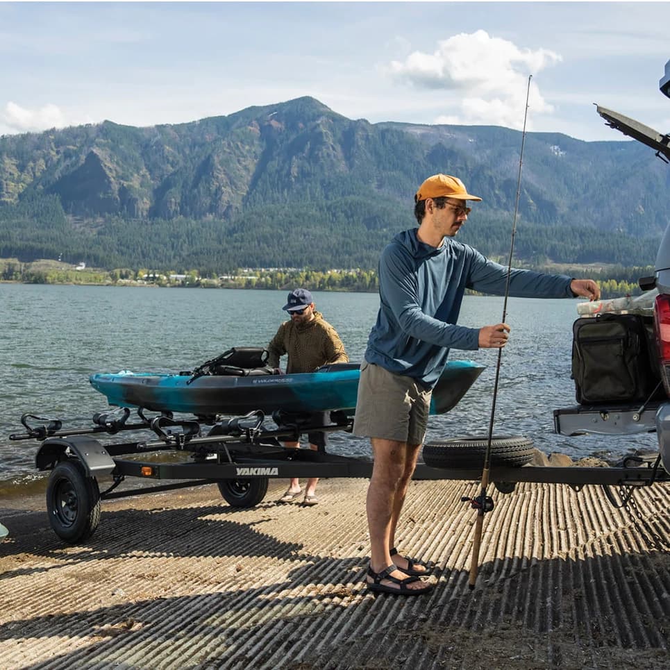 yakima lowrider trailer loaded with a kayak being back up into water with mountains in the background