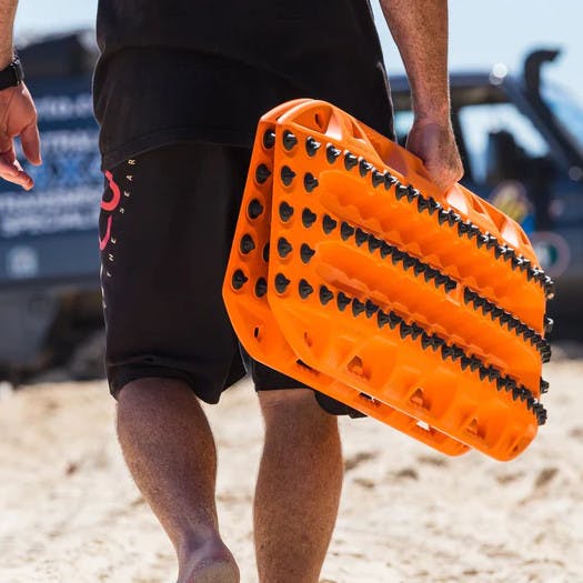 Person walking and holding Maxtrax XTREME Signature Orange recovery boards