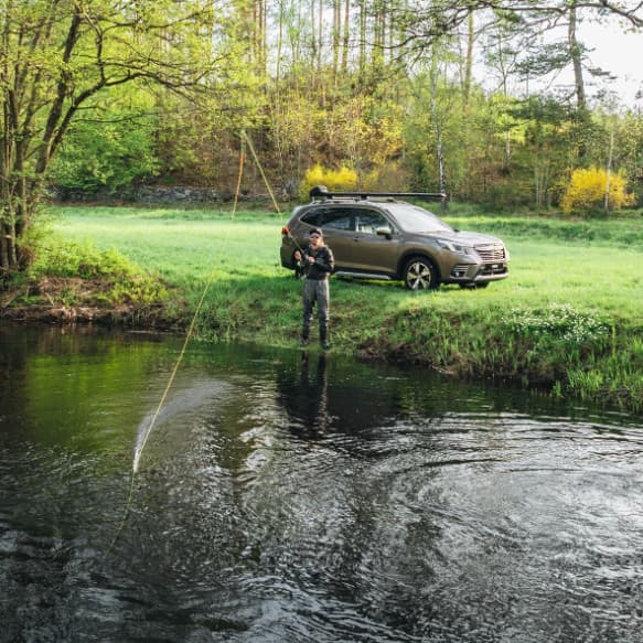 Man fishing in a pond with the SUV behind him that is equipped with the Thule Rod Vault