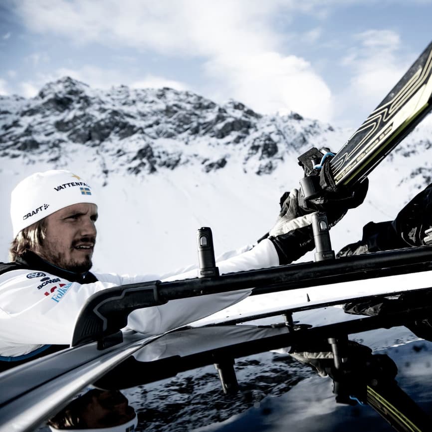 lifestyle image of a man putting their cross-country skis on the skiclick that is installed on the roof of the vehicle. snow and mountain in the background