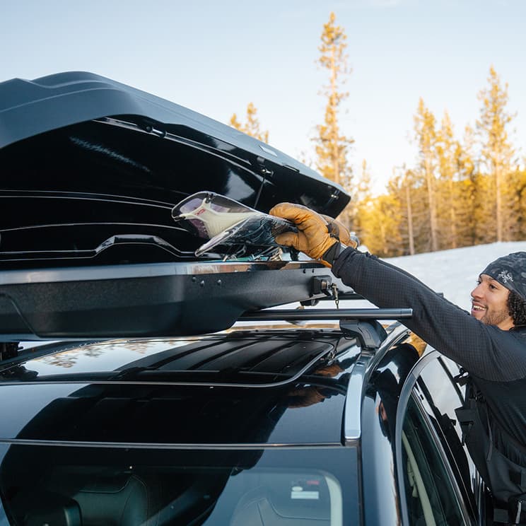 Yakima NX Skinny Cargo box open on top of SUV with person pulling out their skis